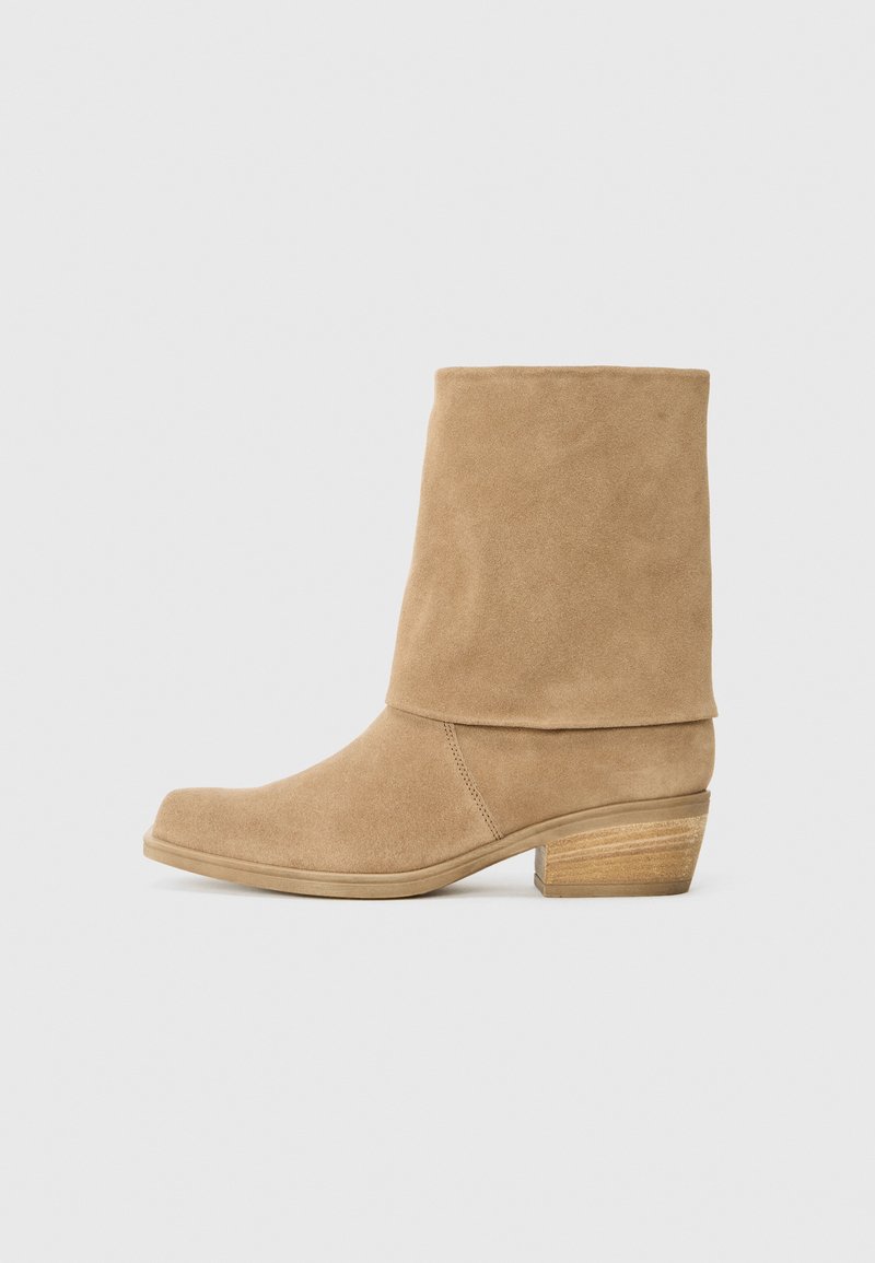 Bottines en suède beige avec un tige repliée, bout arrondi et un talon en bois empilé. Texture lisse, design minimaliste, sans matériel visible.