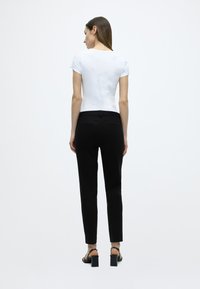 Λευκό τοπ με κοντά μανίκια σε συνδυασμό με μαύρο παντελόνι στενής γραμμής, με ομαλή υφή και απλό σχεδιασμ ό στο πίσω μέρος. Παπούτσια: μαύρα σανδάλια με φαρδύ τακούνι.