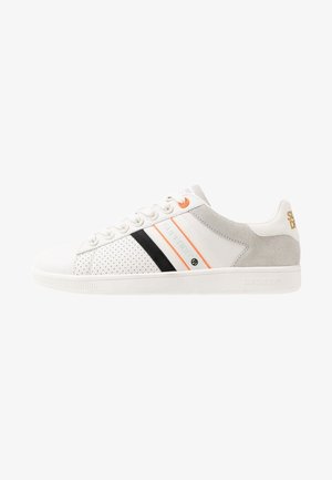 Vit sneaker med perforerade sektioner, svarta och orange ränder, grå mockadetaljer och en texturerad gummisula. Märkning på hälen.