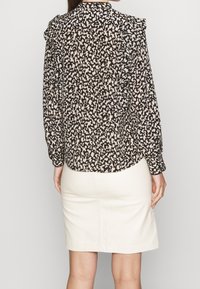 Svart och beige mönstrad blus med ruffle detaljer på axlarna, kombinerad med en figurnära krämfärgad kjol, sedd från baksidan.