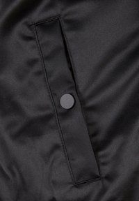 Tissu rembourré noir à texture lisse avec une poche à rabat et un bouton-pression noir. Le design est minimaliste et fonctionnel.