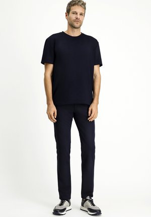 Camiseta azul marino y pantalones tapered a juego, ambos de algodón, con mangas cortas y cuello redondo. Combinado con zapatillas deportivas negras y grises.