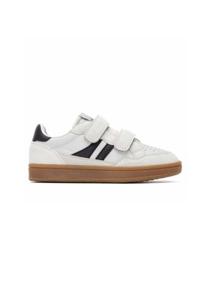 Zapatilla blanca con dos franjas negras, dos tiras de velcro y una suela de goma marrón, mostrada en perfil izquierdo sobre fondo blanco.