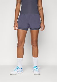 Donkergrijze sportshorts met een eenvoudig ontwerp, voorzien van zijzakken en een contrasterende elastische tailleband. Gedragen met witte sokken en sneakers.