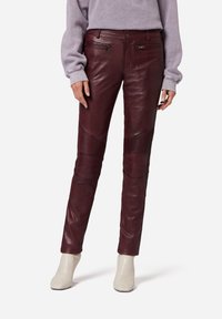 Burgunderfarbene Lederhose mit Panelelementen und Reißverschlusstaschen, im Slim-Fit und mit glatter Textur. Kombiniert mit hellen Ankle-Boots.