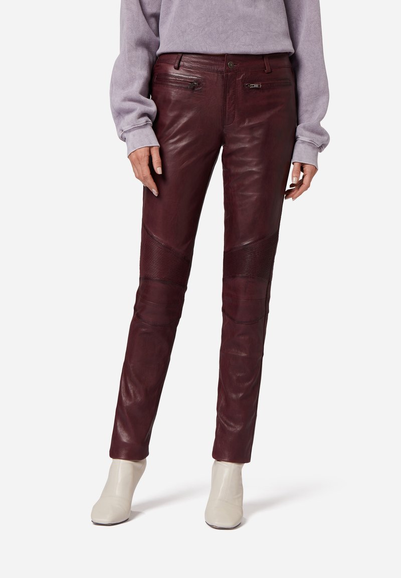 Burgunderfarbene Lederhose mit Panelelementen und Reißverschlusstaschen, im Slim-Fit und mit glatter Textur. Kombiniert mit hellen Ankle-Boots.