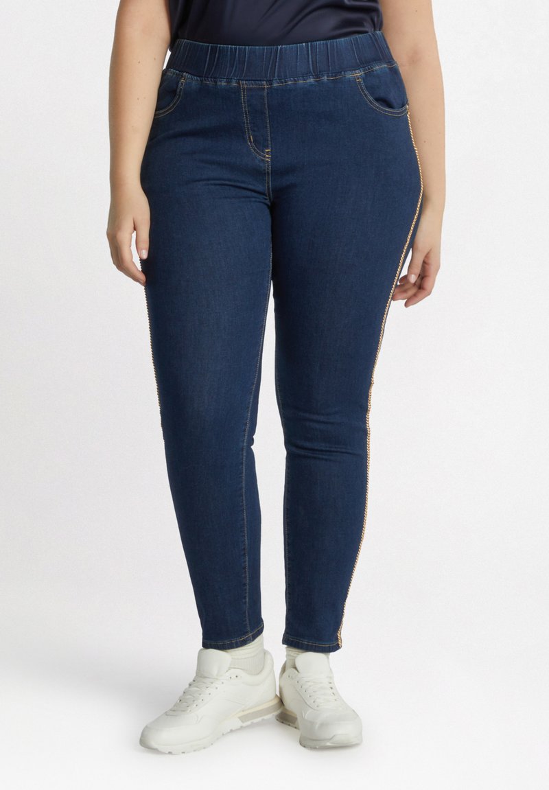Leggings de mezclilla azul oscuro con cintura elástica, bolsillos laterales y costuras de acento dorado a lo largo de las costuras exteriores.