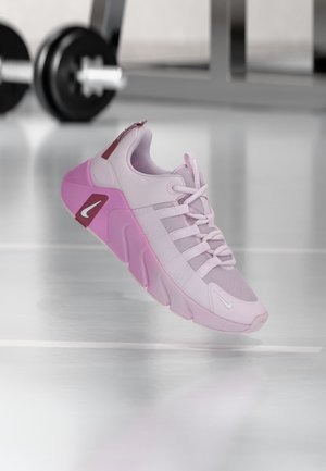 Világoslila és rózsaszín Nike sportcipő vastag talppal, hálós és szövet felsőrész, beltéren kiállítva, háttérben elmosódott súlyzóval.
