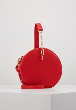 Bolso bandolera circular rojo hecho de material sintético liso. Cuenta con herrajes de tono dorado, correa ajustable y detalle de logo en relieve.