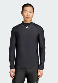 Zwart sportshirt met lange mouwen van synthetisch materiaal, met een ribbelkraag en een klein wit logo op de borst.
