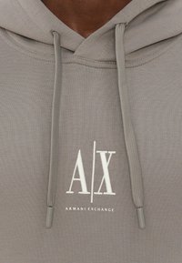 Felpa grigia con cappuccio caratterizzata da un tessuto testurizzato, logo ricamato bianco "A/X" sopra "ARMANI EXCHANGE" e lacci abbinati con estremità in metallo.