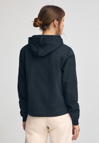 Svart hoodie med en avslappnad passform, med en justerbar huva, ribbade ärmslut och fåll. Tyget ser mjukt ut med en slät struktur.