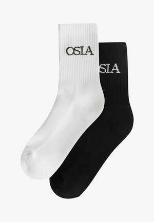 Par de calcetines básicos, uno blanco con texto negro "OSLA" y uno negro con texto blanco "OSLA", mostrados superpuestos sobre un fondo blanco.