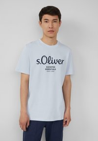 Lichtblauwe katoenen t-shirt met een ronde halslijn en korte mouwen. De voorkant toont "s.Oliver" met daaronder "ELEVATED ESSENTIALS" in donkerblauwe tekst.