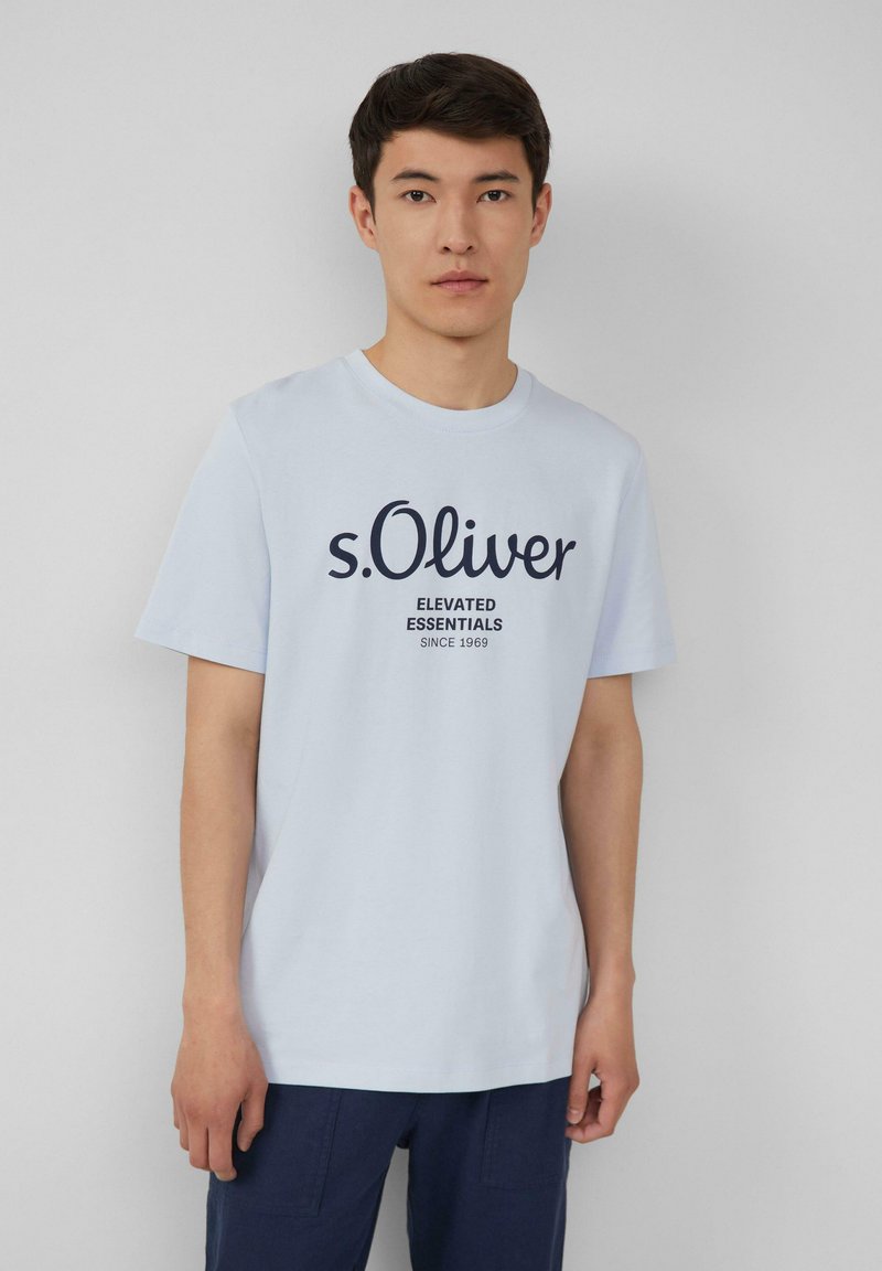 Lichtblauwe katoenen t-shirt met een ronde halslijn en korte mouwen. De voorkant toont "s.Oliver" met daaronder "ELEVATED ESSENTIALS" in donkerblauwe tekst.