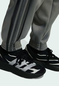 Čierne a biele športové topánky s sieťovinou a zamšovými detailmi, skombinované so šedými teplákmi so striebornými bočnými pruhmi a elastickými manžetami.