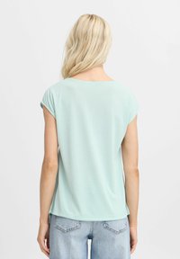 Helles mintgrünes Kurzarmoberteil mit lockerem Schnitt, rundem Ausschnitt und glatter Textur, kombiniert mit hoch taillierten Jeansshorts.