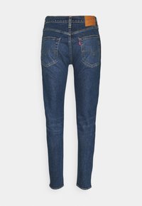 Dark blue denim jeans with a slim fit, standard five-pocket design, and a brown leather patch on the waistband.