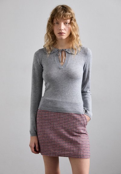 Grau gestrickter Pullover mit Rundhalsausschnitt und Bindungsdetail, kombiniert mit einem enganliegenden Minirock mit rot-blauem Karomuster.