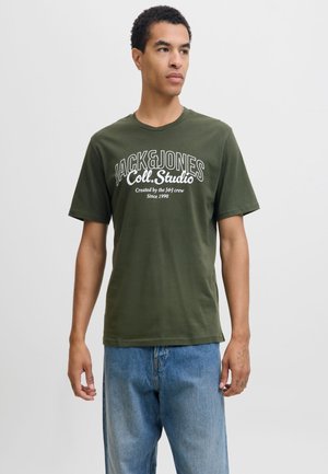Tricou verde măsliniu cu mâneci scurte, realizat din bumbac, cu text alb îndrăzneț "JACK & JONES Coll. Studio" și croială lejeră. Purtați cu blugi albastru deschis.