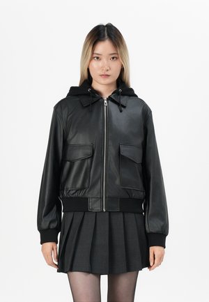 Veste bomber noire en simili cuir avec capuche, fermeture éclair à l'avant, deux poches poitrine, bords côtes aux poignets et à l'ourlet, associée à une jupe plissée foncée.