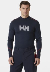 Marineblauwe langoef basislaag met een witte gestreepte "HH" logo, rode accentstiksels op de schouders en een gestructureerde stof op de mouwen.