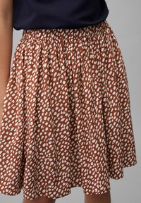 Gonna marrone con vita arricciata, caratterizzata da un motivo a pois bianchi. Realizzata in tessuto leggero, con un design a svaso e lunghezza al ginocchio.