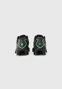 Black athletic shoes with a smooth finish, featuring green accents, padded collar, and a springy sole design for support.