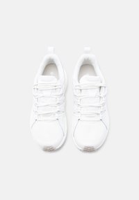 Ζευγάρι λευκών αθλητικών παπουτσιών με κορδόνια, τοποθετημένα δίπλα-δίπλα σε ανοιχτό φόντο, σε θέα από πάνω.