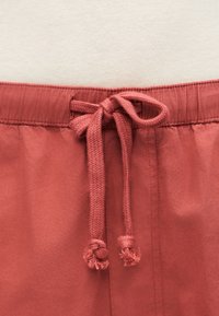 Nærbillede af bundet lyserødt stofsnøre på matchende elastisk linning på bløde bukser eller shorts.