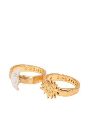 Dos anillos de oro con pequeñas figuras de sol y luna creciente con rostros sobre un fondo blanco.