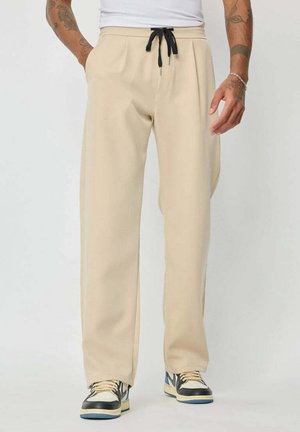 Pantalons de survêtement beige en tissu doux avec une coupe décontractée, dotés d'un cordon noir, de poches latérales et de bas de jambe fuselés.