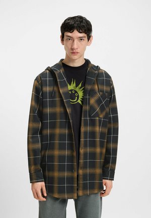 Sort og orange ternet skjorte med hætte, med knaplukning foran og en brystlomme, båret over en sort grafisk t-shirt.