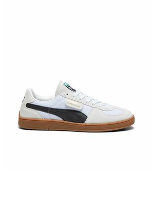 Zapatilla blanca y gris con una franja lateral negra, suela de goma, diseño de cordones y detalles de logo en el lateral. Incluye materiales texturizados.