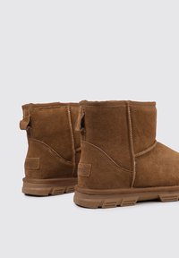 Bottines en daim marron avec une texture lisse, une forme arrondie et une semelle en caoutchouc robuste. Elles disposent d'une languette à l'arrière pour un enfilement facile.
