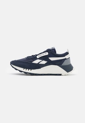 Baskets Reebok bleu marine et blanches avec dessus en daim et mesh, semelle épaisse et détails de marque sur le côté et la languette.