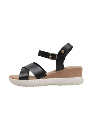 Sandales compensées en cuir noir avec des sangles croisées, détail de boucle et une semelle texturée blanche. Le talon est légèrement surélevé avec un insert beige.