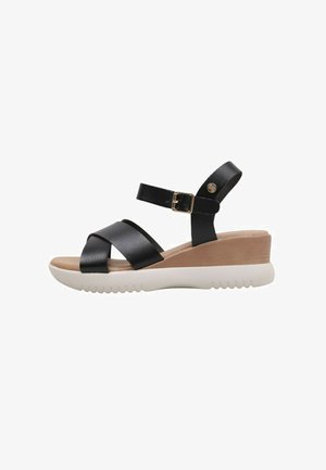 Sandales compensées en cuir noir avec des sangles croisées, détail de boucle et une semelle texturée blanche. Le talon est légèrement surélevé avec un insert beige.