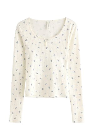 Vit långärmad topp med ribbat mönster, med ett litet blått blommönster och rundad halsringning med stängning med två knappar.