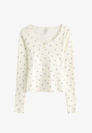 Valkoinen pitkähihaisen paidan, jossa on ribbetty rakenne, pienen sinisen kukkakuviot ja pyöreä kaula-aukko, jossa on kaksipainikekiristys.