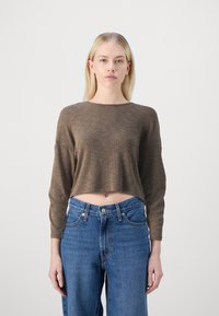 Top marron côtelé, court à manches longues, associé à un jean bleu taille haute, avec poches avant et fermeture à bouton.