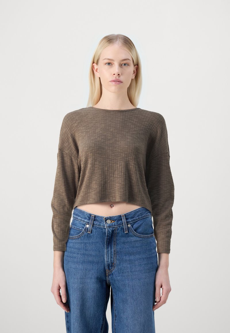 Top marron côtelé, court à manches longues, associé à un jean bleu taille haute, avec poches avant et fermeture à bouton.