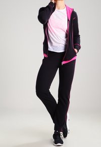 Black zip-up jacket with pink accents, paired with a white T-shirt and black pants. Lightweight, sporty fabric with a relaxed fit.