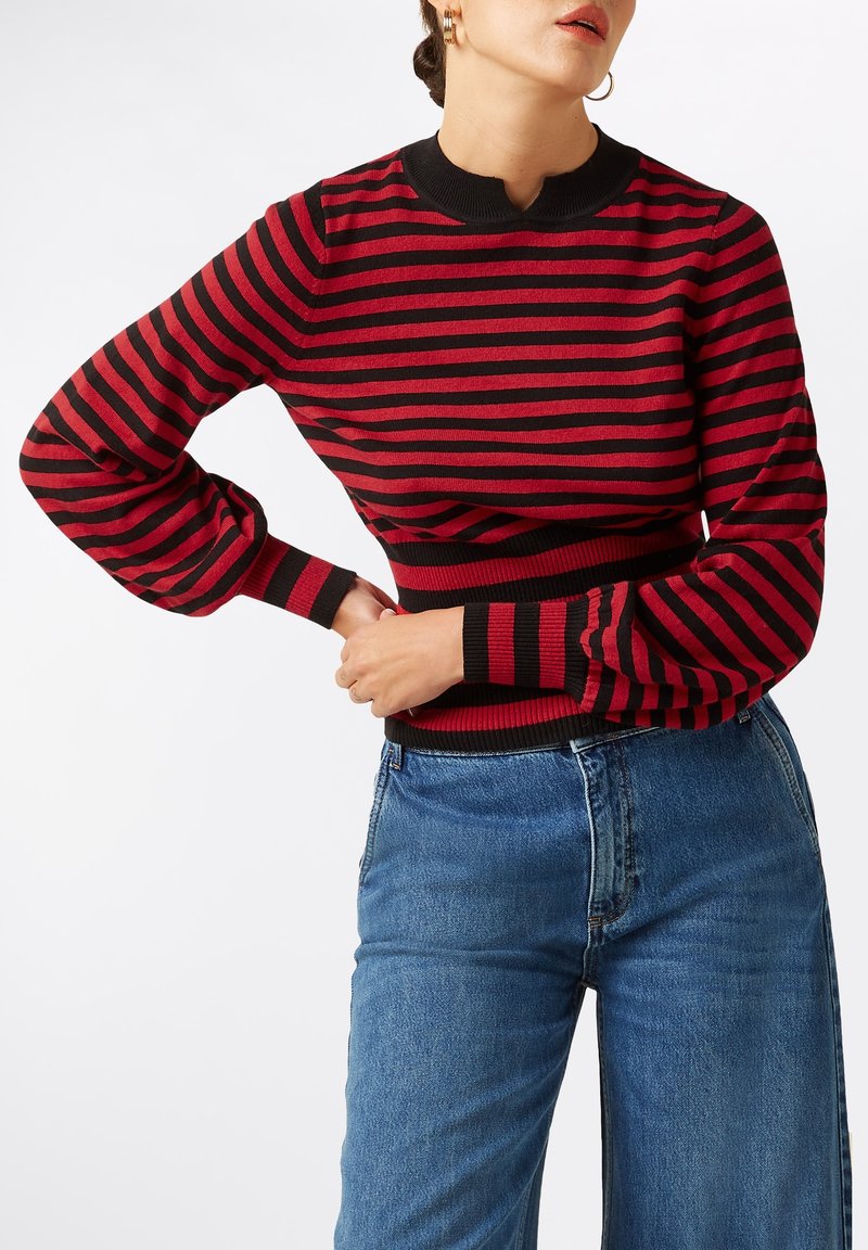 Rot-schwarz gestreifter Pullover mit geripptem Saum und Bündchen, ausgestattet mit einem hohen Kragen und Ballonärmeln. Kombiniert mit blauen Jeans.