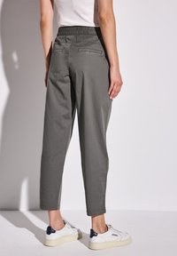 Grijze, relaxte broek met een elastische tailleband, voor- en achterzakken, en omgeslagen zomen, gedragen met witte en marineblauwe sneakers.