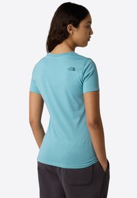 Lyseblå kortærmet T-shirt lavet af blødt stof, med et lille gråt logo på den øverste ryg og en tætsiddende design.