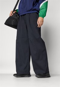 Pantaloni a gamba larga blu navy realizzati in un tessuto leggero con un motivo testurizzato, abbinati a sneakers nere e a una borsa nera.
