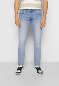 Světle modré džíny z denimu s úzkým střihem, vybavené klasickým designem s pěti kapsami a jemným vyblednutím. Doplněné černobílými teniskami.