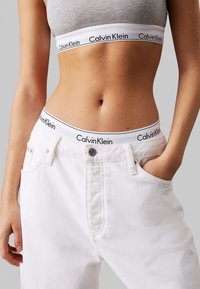 Pantalones de mezclilla blancos de talle alto con un diseño de cinco bolsillos, que presentan un botón plateado y costuras de contraste, combinados con un top corto gris.