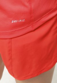 Punaiset Dri-FIT -shortsit, joissa on sileä pinta, ommeltu helma ja valkoinen logo. Kevyt ja kosteutta siirtävä urheilumateriaali.